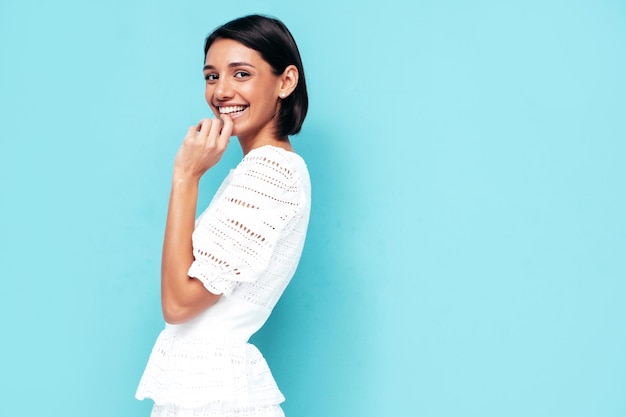 Young beautiful smiling female in trendy summer white dress Sexy carefree woman posing near blue wall in studio Positive model having fun Cheerful and happy Isolated