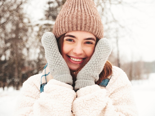 Молодая красивая улыбающаяся хипстерская женщина в модной теплой одежде и шарфе. Беззаботная женщина позирует на улице в парке. Позитивная чистая модель развлекается в снегу. Наслаждаясь зимними моментами