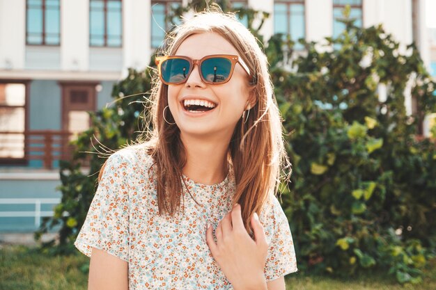 トレンディな夏の服を着た若い美しい笑顔の流行に敏感な女性日没で通りの背景にポーズをとるセクシーな屈託のない女性屋外のポジティブモデルサングラスで陽気で幸せ