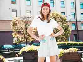 Free photo young beautiful smiling hipster woman in trendy summer white tshirt sexy carefree woman posing on the street background in cap at sunset positive model outdoors cheerful and happy