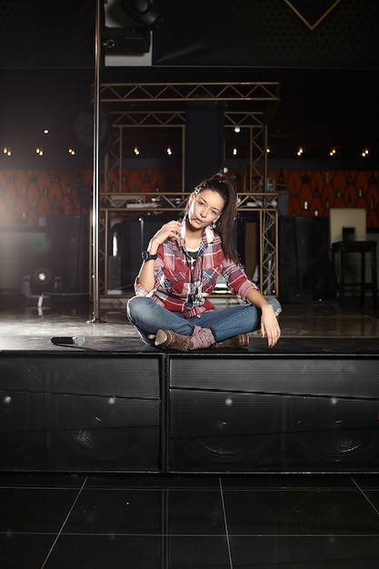 young beautiful smiling pop star singer with microphone sitting on the scene in the club