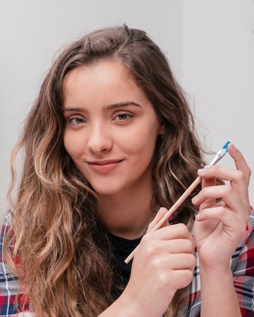 Young beautiful smiling woman holding paintbrush looking at camera