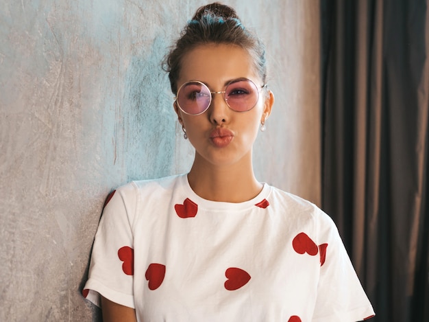 Young beautiful smiling woman looking at camera  Trendy girl in casual summer white dress and sunglasses    Making duck face