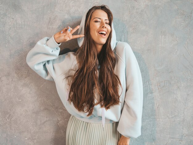 Young beautiful smiling woman looking . Trendy girl in casual summer hoodie and skirt clothes.  . Showing peace sign