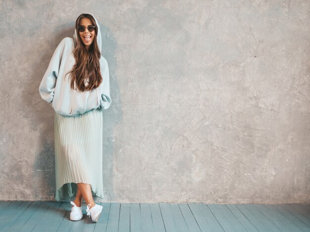 Young beautiful smiling woman looking . Trendy girl in casual summer hoodie and skirt clothes.   showing tongue