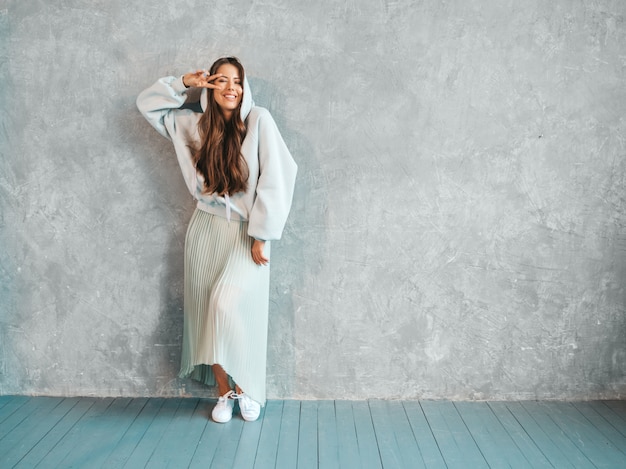 Young beautiful smiling woman looking . Trendy girl in casual summer hoodie and skirt clothes.  .Shows peace sign