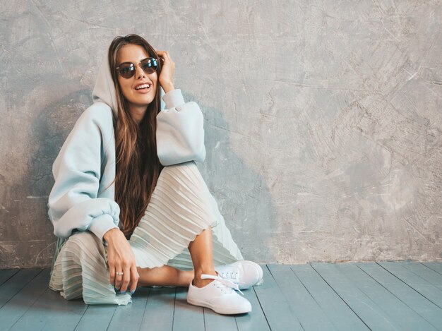 Young beautiful smiling woman looking . Trendy girl in casual summer hoodie and skirt clothes.   sitting on the floor