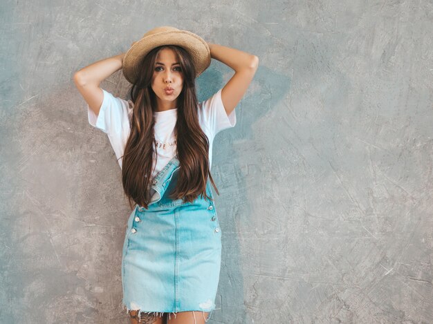 Young beautiful smiling woman looking . Trendy girl in casual summer overalls clothes and hat. . Giving kiss