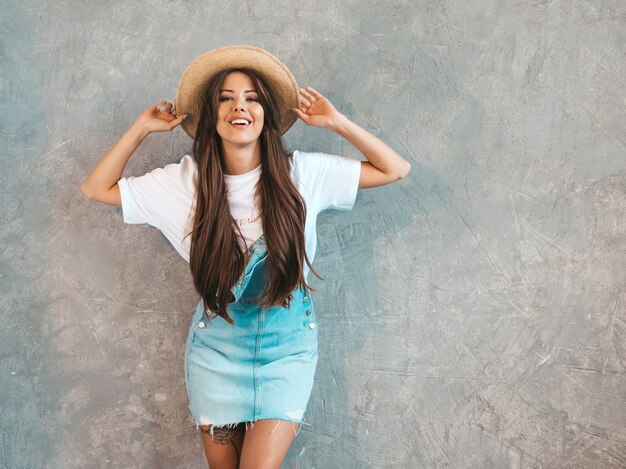Young beautiful smiling woman looking . Trendy girl in casual summer overalls clothes and hat. 