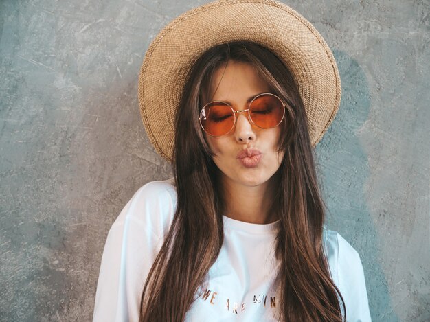 Young beautiful smiling woman looking . Trendy girl in casual summer t-shirt clothes and hat.. Giving air kiss