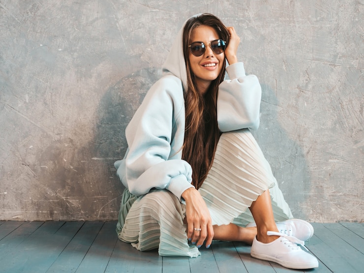 Free Photo young beautiful smiling woman shows peace sign. trendy girl in casual summer hoodie and skirt clothes.   sitting on the floor
