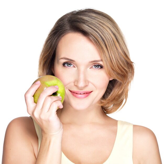 若い美しい笑顔の女性は、白で隔離された顔にリンゴに触れます。