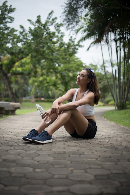 若い美しいスポーツの女性は、ジョギング後に公園に座る。健康とスポーツのコンセプト。