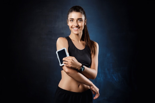 Young beautiful sportive girl posing over dark wall.