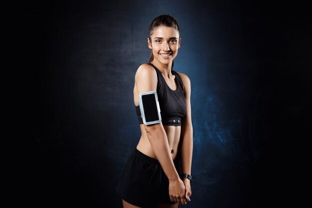 Young beautiful sportive girl posing over dark wall.