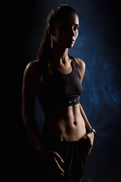 Young beautiful sportive girl posing over dark wall.