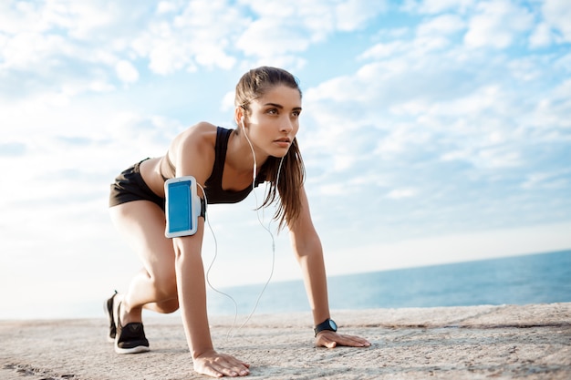 Young beautiful sportive girl preparing to run over seaside.