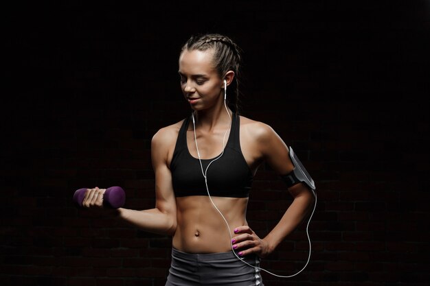 Young beautiful sportive girl smiling, training over dark wall