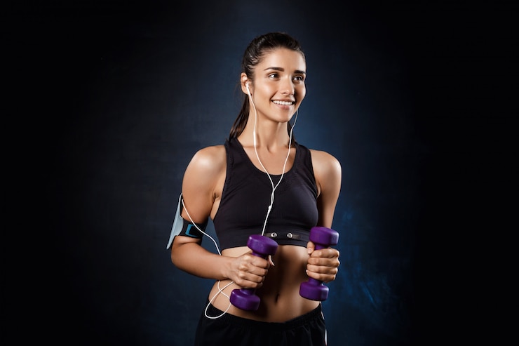 Free Photo young beautiful sportive girl training with dumbbells over dark wall.