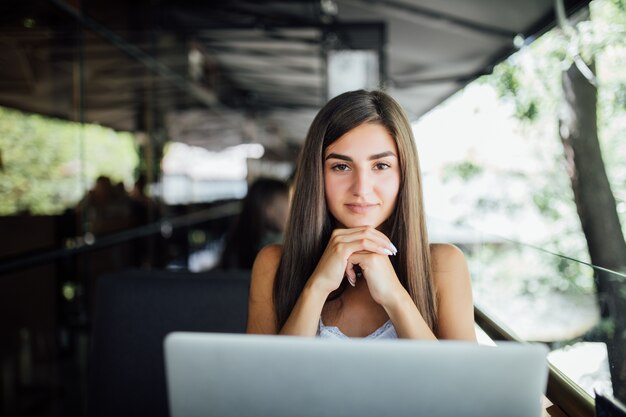 ノートパソコンとカフェでお茶やコーヒーのカップを持つ若い美しい学生の女の子