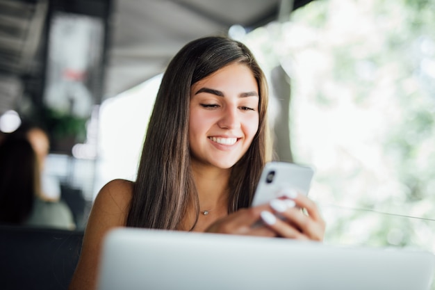 Ragazza giovane bella studentessa con il computer portatile e una tazza di tè o caffè nella caffetteria