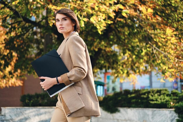 Young beautiful stylish businesswoman with folder thoughtfully walking on city street