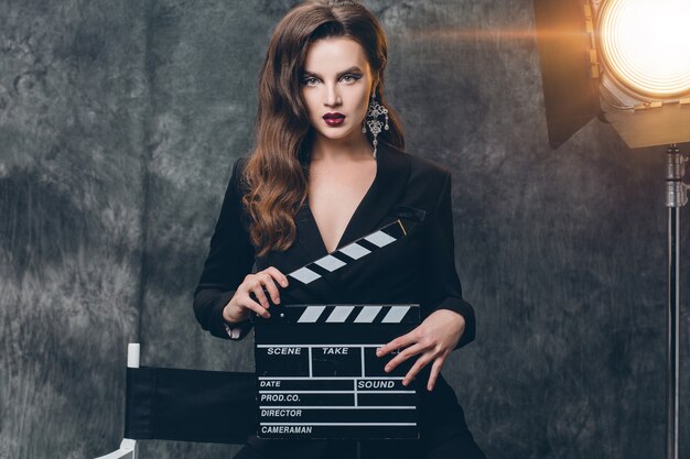 Young beautiful stylish sexy woman on cinema backstage, holding movie clapper