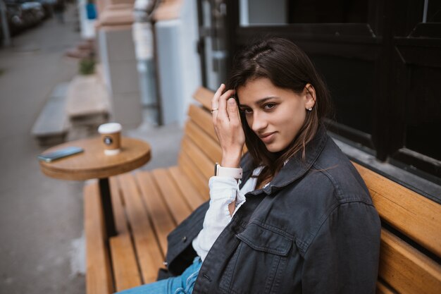 Молодая красивая стильная женщина, сидя на улице скамейке