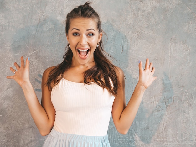 Young beautiful surprised woman looking  with hands in the air. Trendy girl in casual summer clothes. Female posing near gray wall 