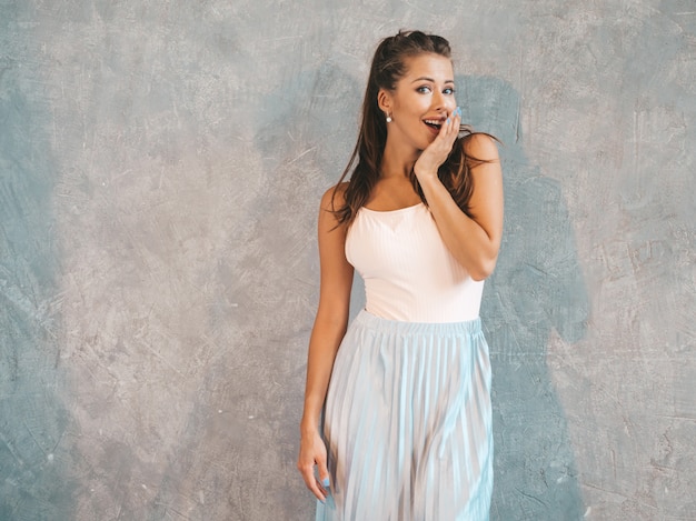 Young beautiful surprised woman looking  with hands near face. trendy girl in casual summer clothes. female posing near gray wall