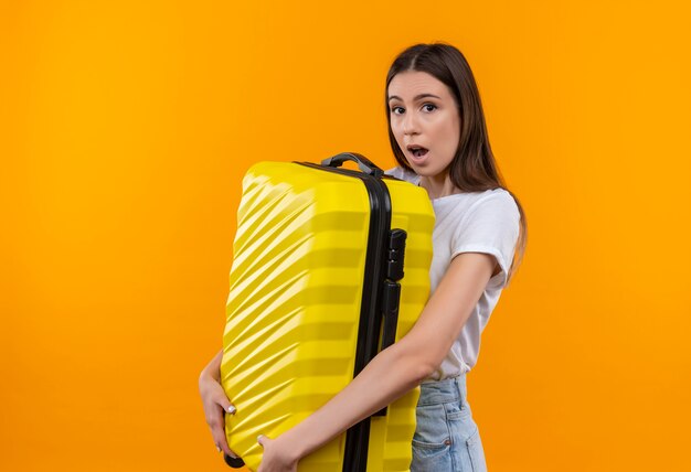 Молодая красивая девушка путешественника держит чемодан, глядя удивлен и поражен