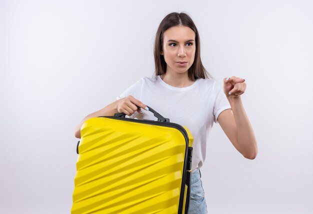 Young beautiful traveler girl holding suitcase looking surprised pointing with index finger to the side 