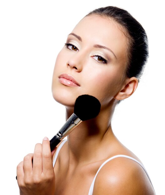 Young beautiful woman applying powder on cheekbone with brush - isolated