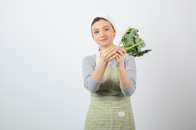 Young beautiful woman in apron holding fresh broccoli on white 