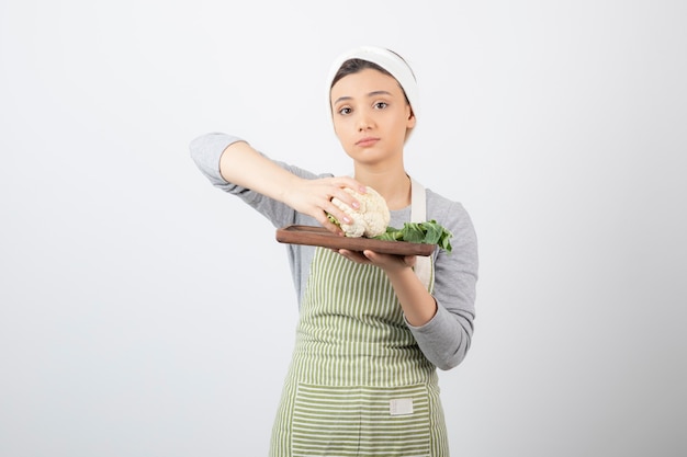 Young beautiful woman in apron holding plate of cauliflower