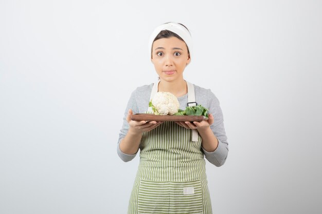 Young beautiful woman in apron holding plate of cauliflower