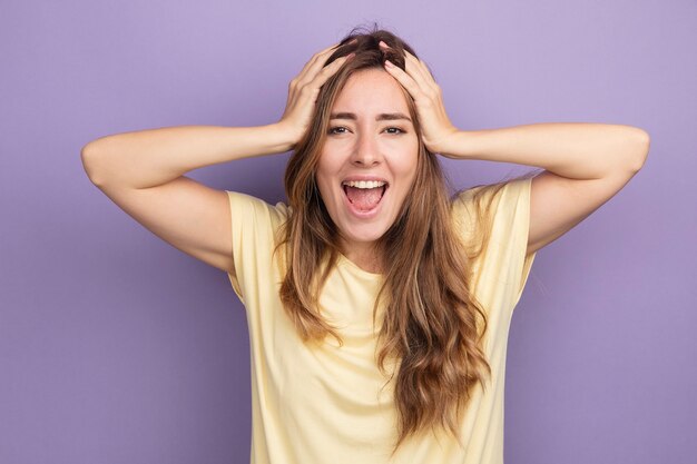 手でカメラを見て興奮して幸せなベージュのTシャツの若い美しい女性