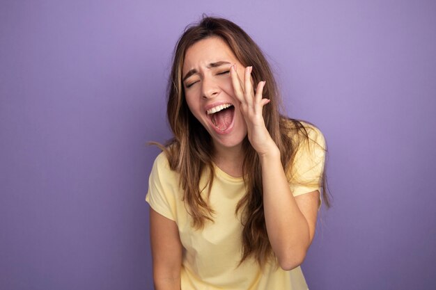 Young beautiful woman in beige t-shirt excited and happy shouting with hand near mouth 