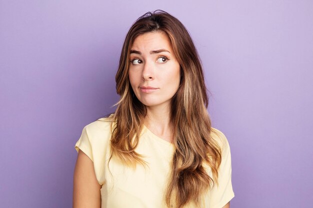 Young beautiful woman in beige t-shirt looking aside with skeptic expression 