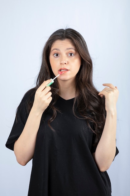 Young beautiful woman in black outfit applying lipstick . 