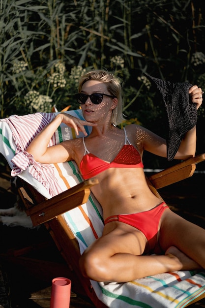 Free photo young beautiful woman in a black straw hat and red swimsuit, sunglasses sunbathing on a sun lounger, the concept of outdoor recreation.