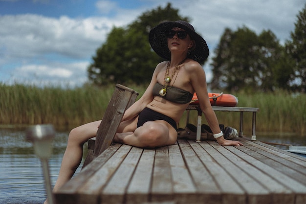 黒い麦わら帽子をかぶった若い美しい女性は、湖のそば、水辺の屋外で夏にリラックスします