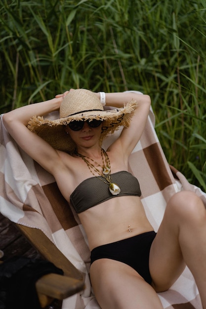 молодая красивая женщина в черной соломенной шляпе отдыхает летом на открытом воздухе у озера, у воды