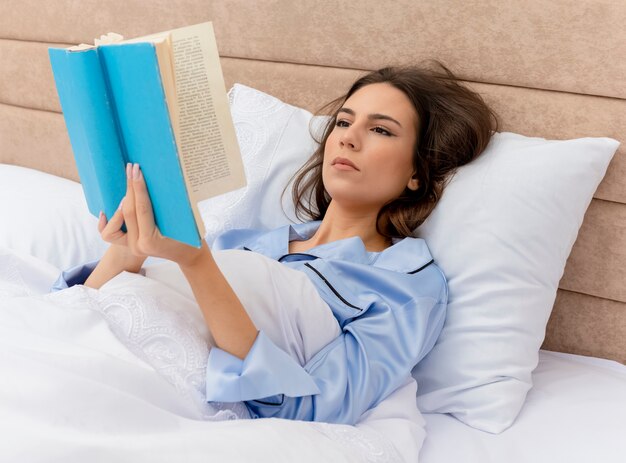 Young beautiful woman in blue pajamas laying on bed