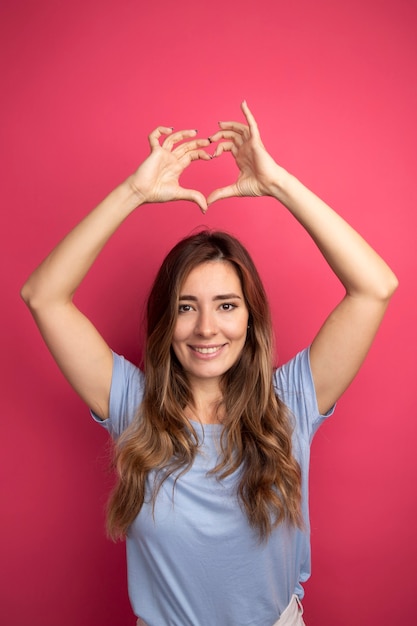 Foto gratuita giovane bella donna in maglietta blu che fa il gesto del cuore sopra la sua testa sorridendo allegramente