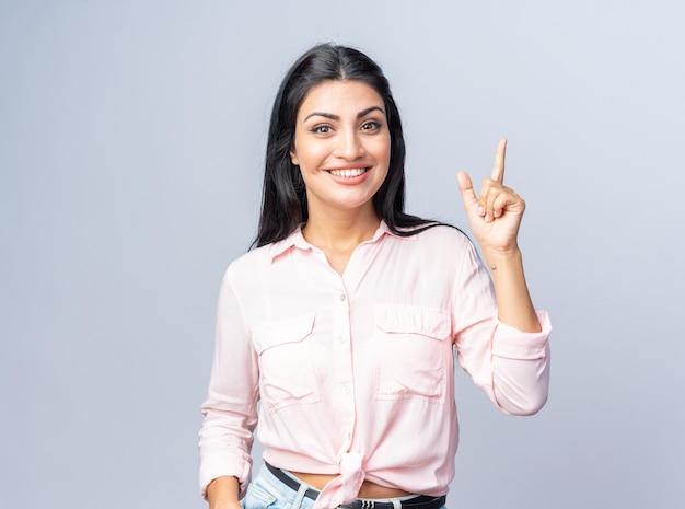 Young beautiful woman in casual clothes  happy and positive smiling cheerfully showing index finger having new great idea standing over white wall