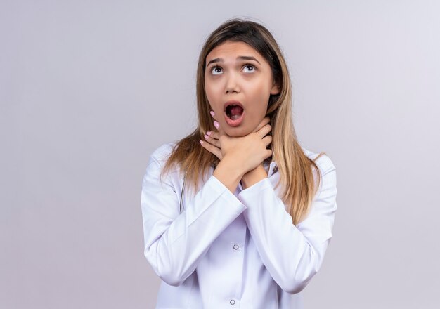 Free photo young beautiful woman doctor wearing white coat with stethoscope choking in panic holding hand around her neck