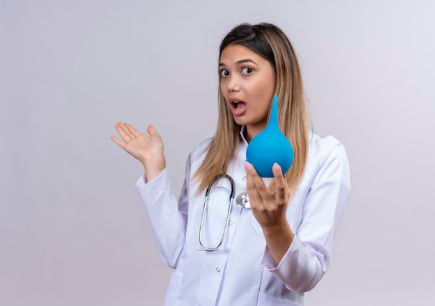 Young beautiful woman doctor wearing white coat with stethoscope holding an enema