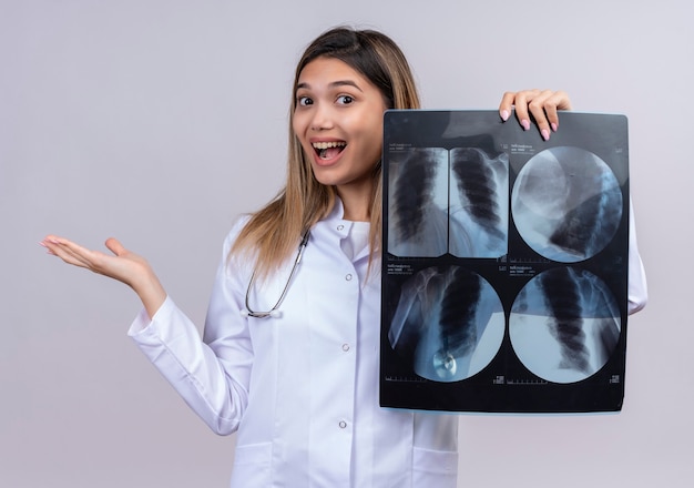 Free photo young beautiful woman doctor wearing white coat with stethoscope holding x-ray of lungs