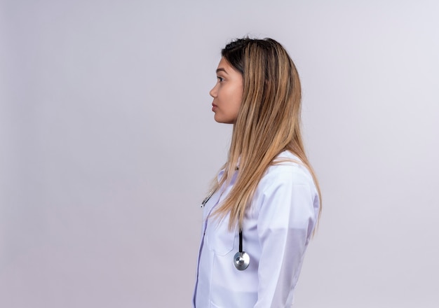 Free photo young beautiful woman doctor wearing white coat with stethoscope standing sideways with serious face